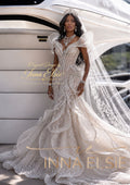 A woman wearing an ornate ivory lace wedding gown with dramatic ruffled shoulders, a fitted bodice, and a long sheer veil, posed in front of a white yacht. Gold text overlays read 'Original Design by Inna Elsie' and 'INNA ELSIE'.