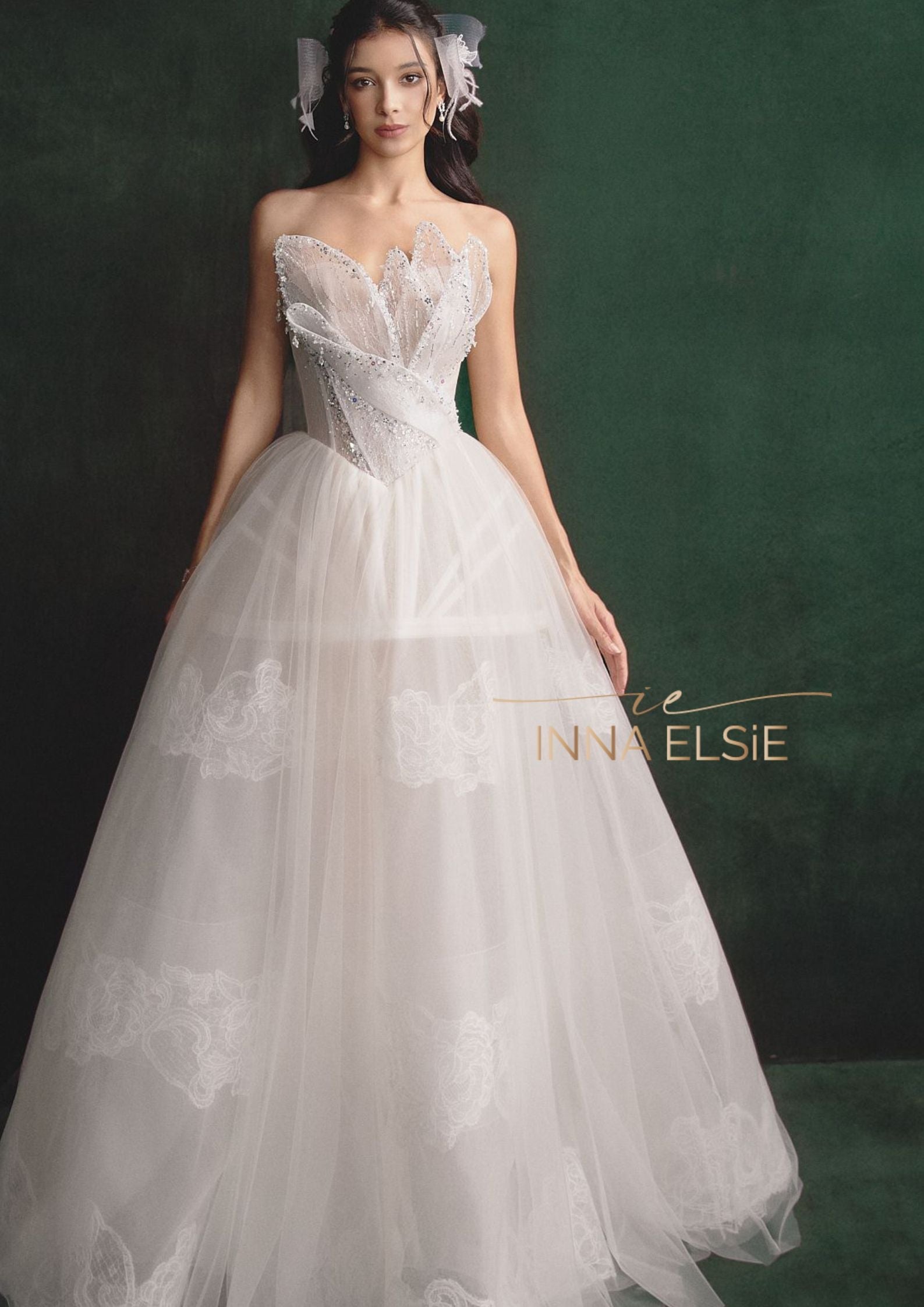 Woman wearing a white lace wedding dress with 'Inna Elsie' branding on a dark green background