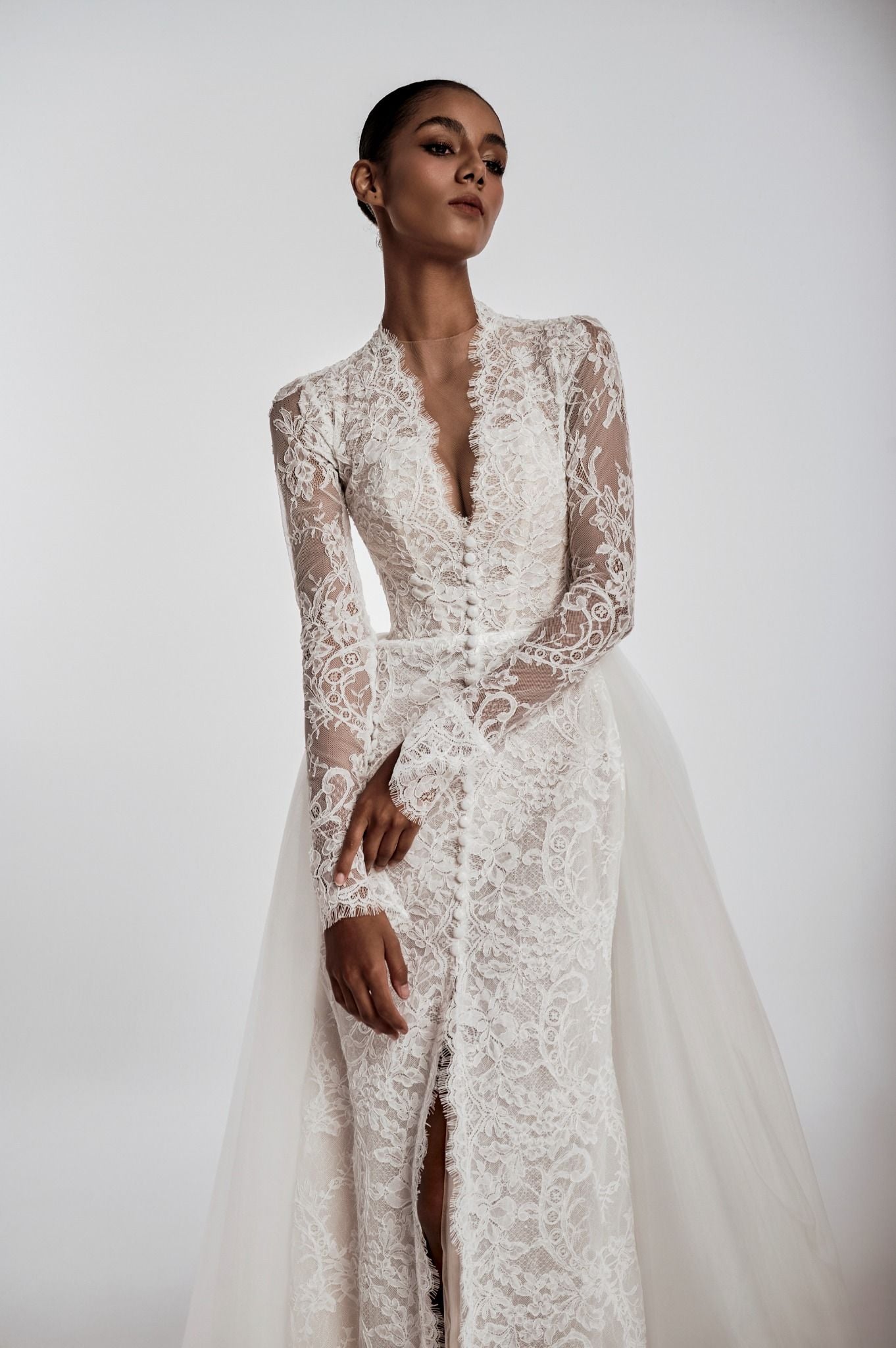 Model wearing a lace wedding dress with long sleeves and a deep neckline on a white background