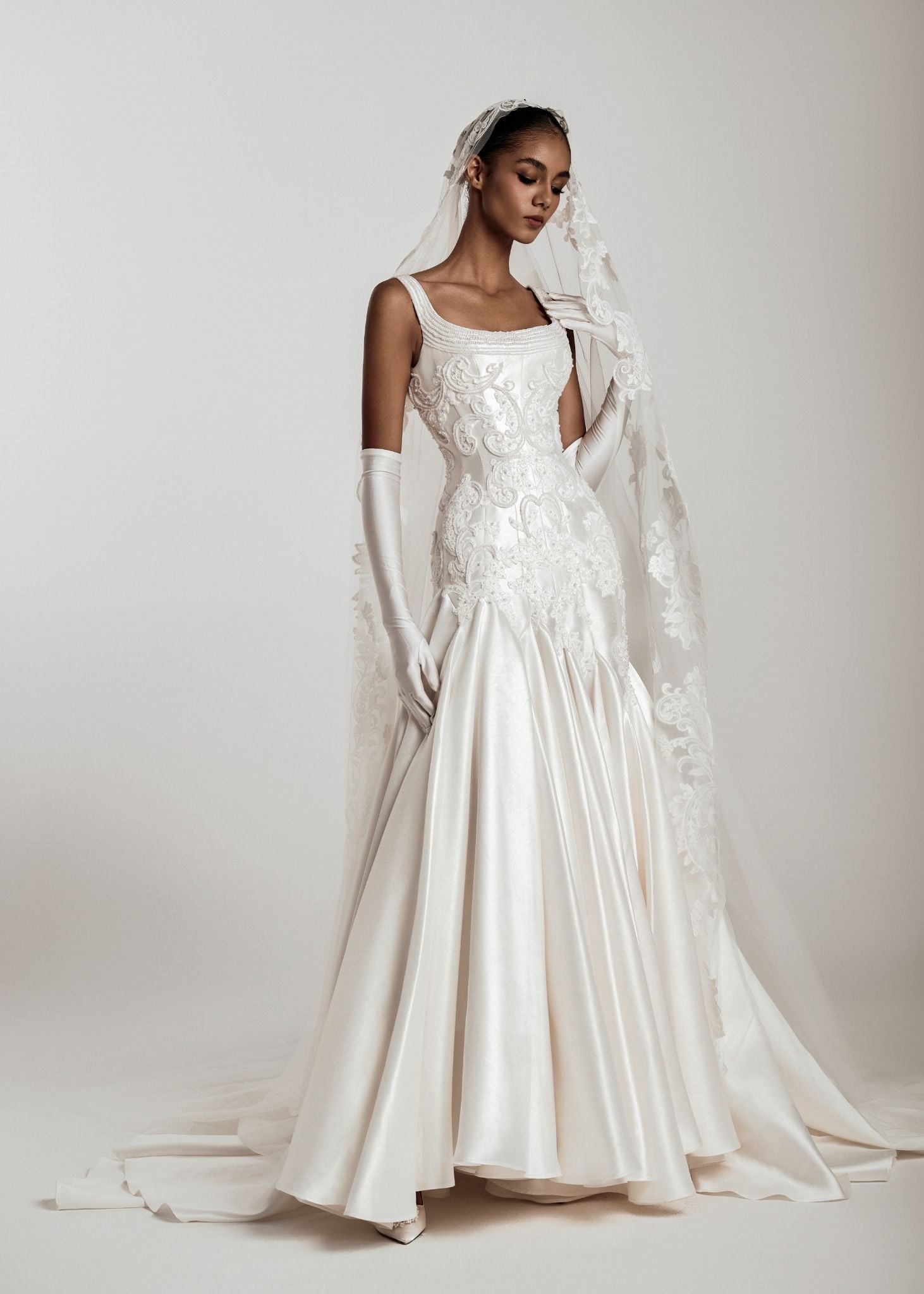 Woman in a white wedding dress with a long train and veil on a plain background