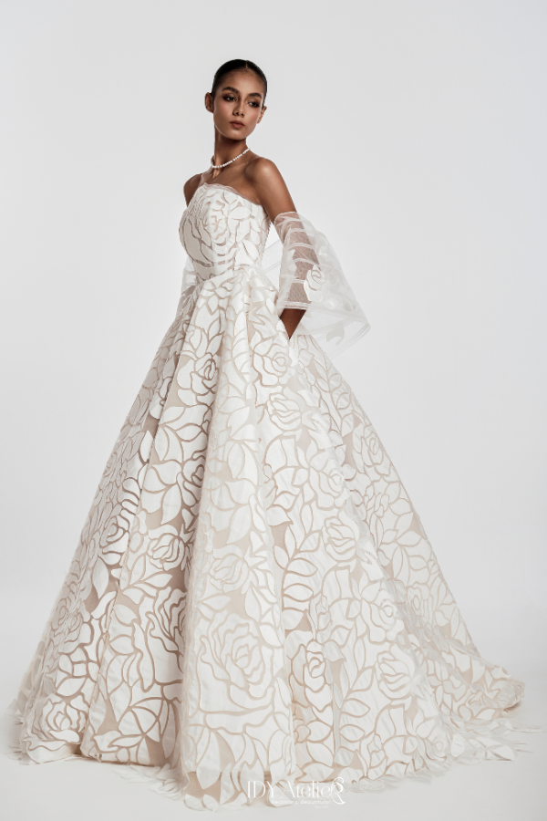 Woman wearing a white lace wedding dress with sheer sleeves on a light gray background