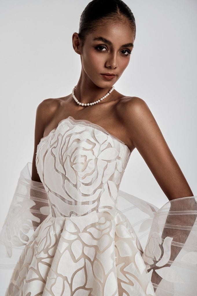 Woman wearing a white floral wedding dress with sheer sleeves on a plain background