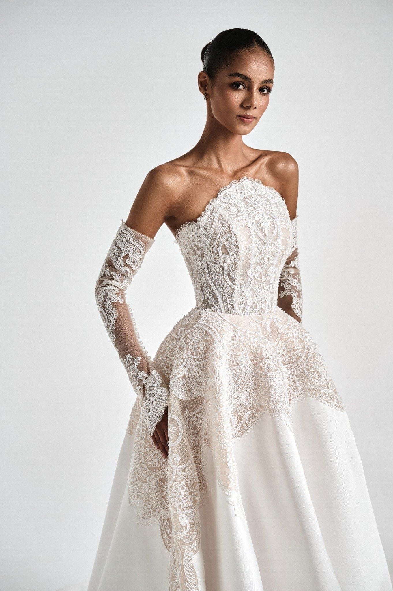 Model wearing a white lace wedding dress with long sleeves on a plain background