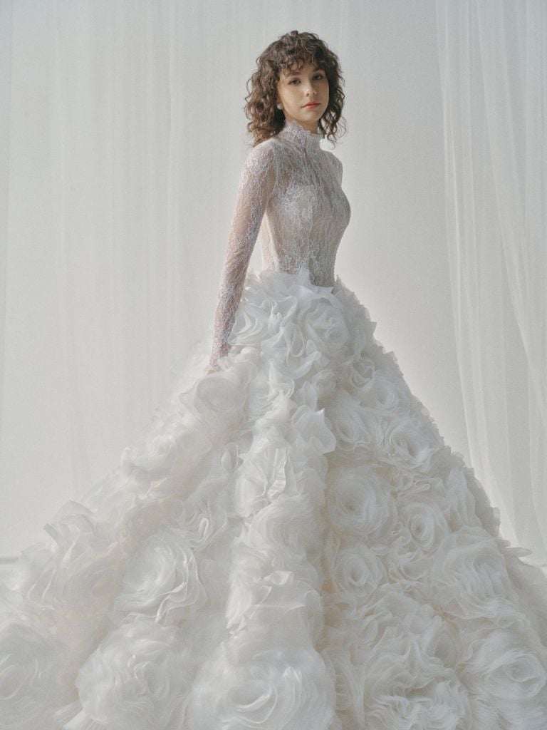 Woman wearing a white wedding dress with floral details against a white background