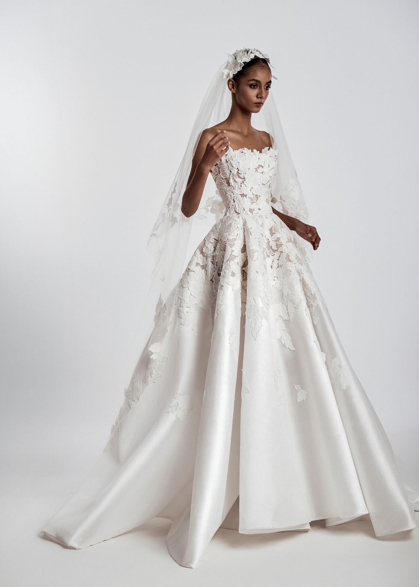 White wedding dress with lace detailing and a veil on a white background
